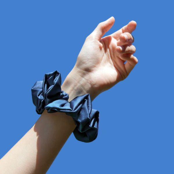 Blauer Seiden-Scrunchie am Handgelenk vor strahlend blauem Himmel – stilvoll, luftig und perfekt für dein natürliches Sommer-Feeling.