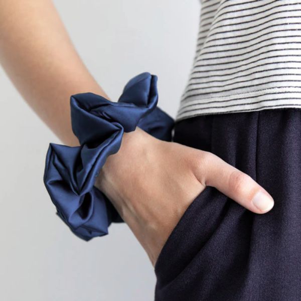 Blauer Seiden-Scrunchie am Handgelenk, kombiniert mit blauer Hose und gestreiftem Pulli – lässiger Look mit Stil und Statement.